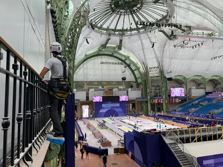 Cordiste ALPITEC suspendu à la structure en fonte du Grand Palais, vue plongeante sur le plateau des Jeux Olympiques Paris 2024 en contrebas