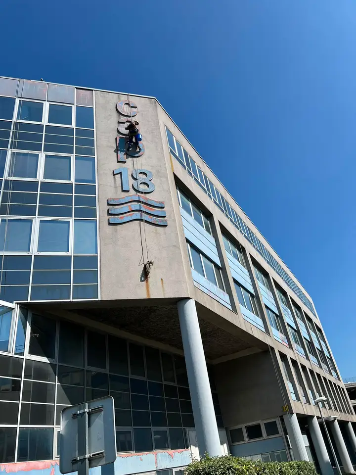 Cordiste suspendu à l'angle d'un immeuble de bureaux, intervenant sur les lettres de l'enseigne en façade