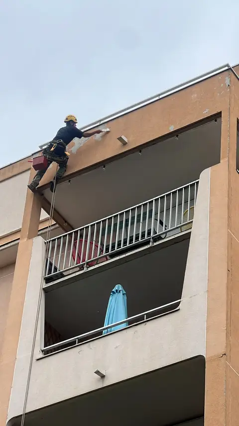 Cordiste au travail sur la façade d'un immeuble résidentiel, réalisant des réparations d'enduit et de maçonnerie au niveau des balcons