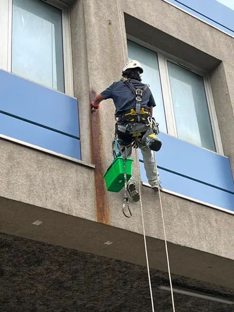 Cordiste intervenant sur des traces de coulures et dépôts sur une façade d'immeuble