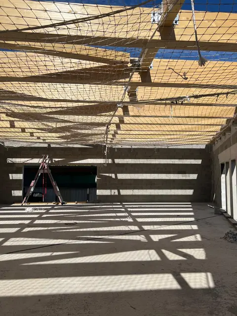 Filet de sécurité tendu sous les poutres bois d'un bâtiment en construction, murs en parpaing bruts