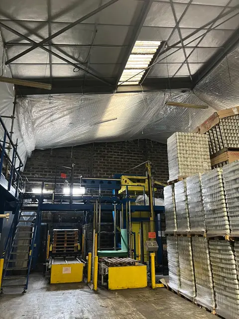 Filet et bâche de confinement suspendus sous la charpente métallique d'un entrepôt en activité, palettes stockées en contrebas