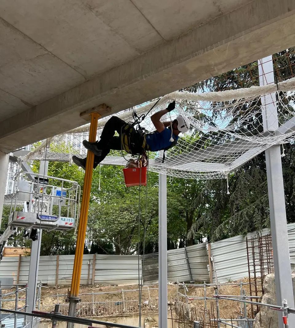 Filet de sécurité horizontal tendu sous une charpente en bois, vu en contre-plongée sur ciel bleu