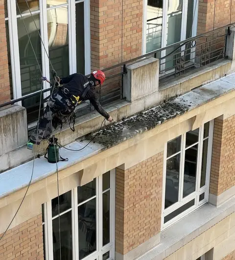 Cordiste appliquant un traitement anti-mousse au pulvérisateur sur le rebord d'une façade en brique