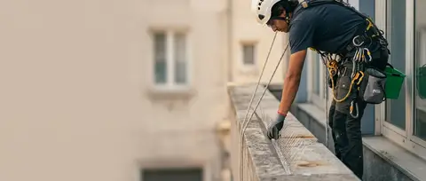 Cordiste sécurisé sur cordes ajustant un dispositif de protection anti-pigeons sur un bandeau de façade